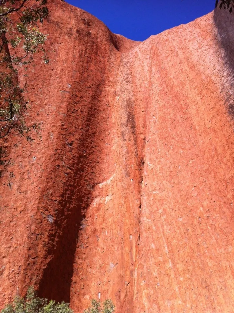 Parete verticale di arenaria rossa di Uluru ripresa dal sentiero alla base